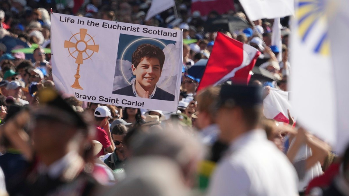 crowd holding banner with picture of Carlo Acutis