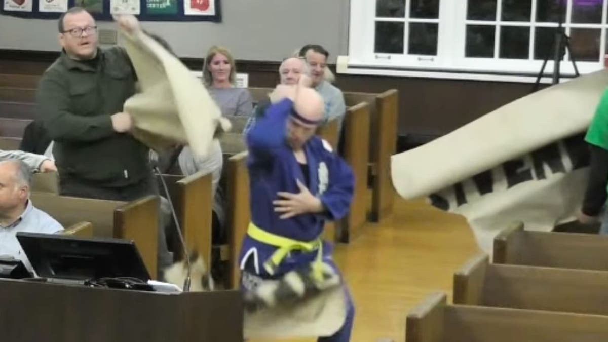 Will Thilly punches through a protest sign during a kung fu-themed demonstration at a Cranford town meeting.