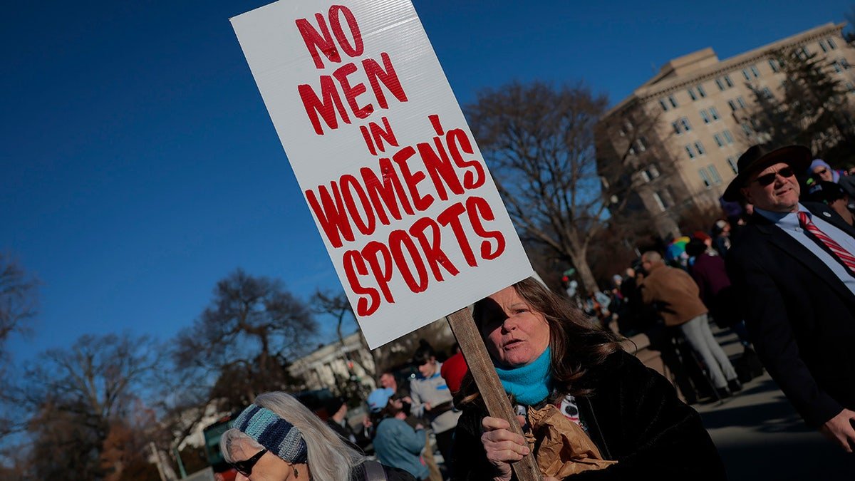 A woman holds a "No men in women's sports" sign