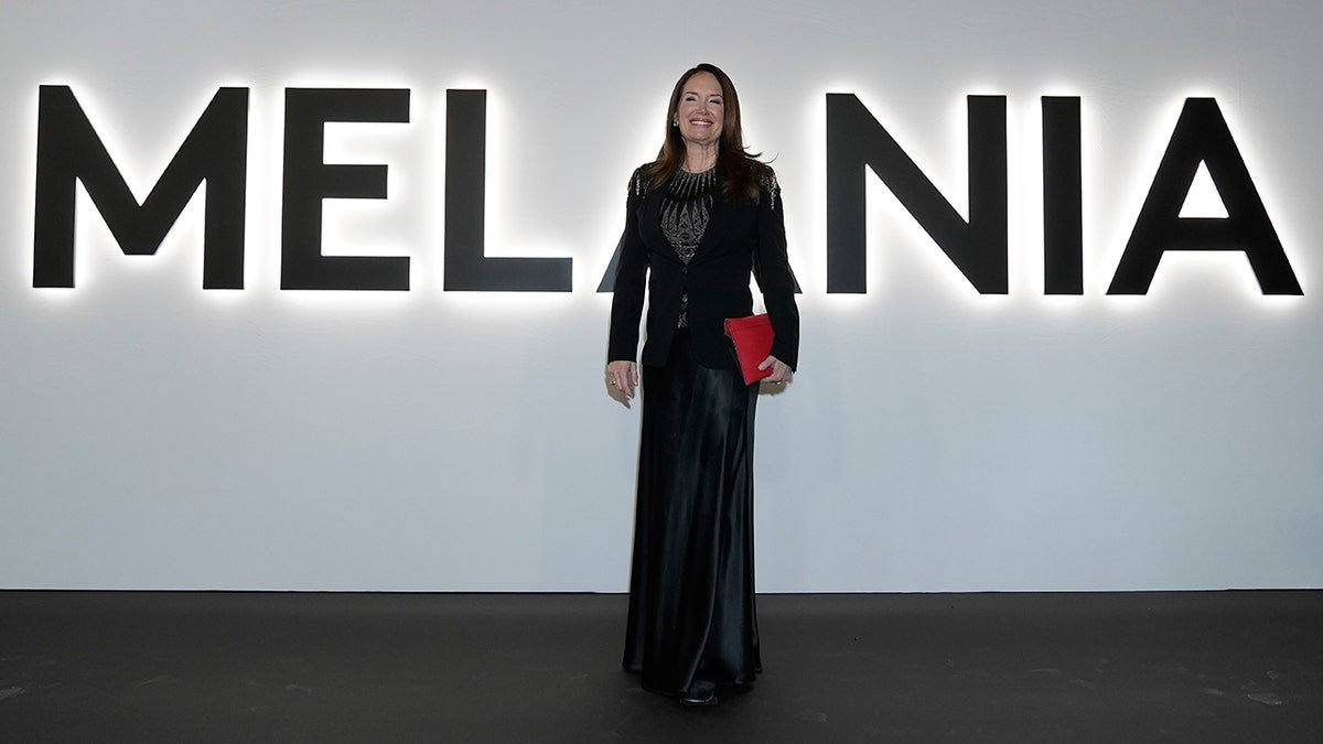 Brooke Rollins wearing a black embellished dress and blazer and holding a red clutch at the red carpet "Melania"