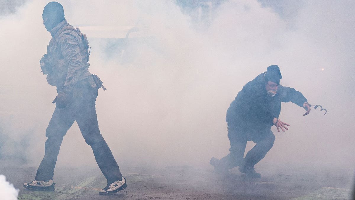 A man wearing handcuffs running through a cloud of tear gas.
