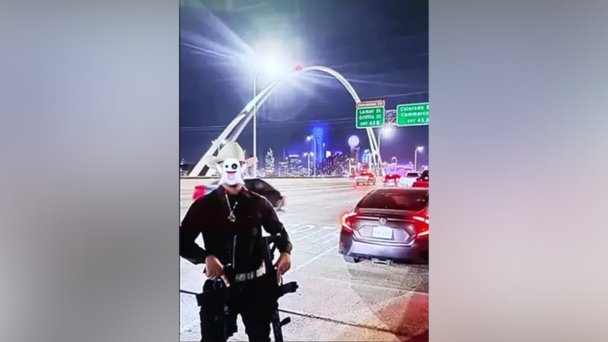 A person is seen holding a firearm on a bridge in Dallas at night