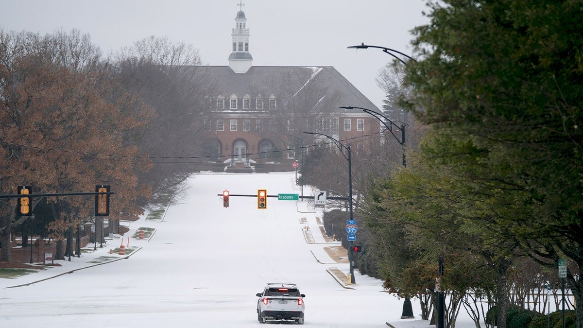 Police vehicle sits at traffic light during winter storm